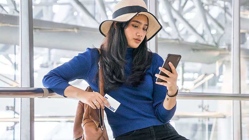 A woman at the airport pays for something on her phone with a Visa card